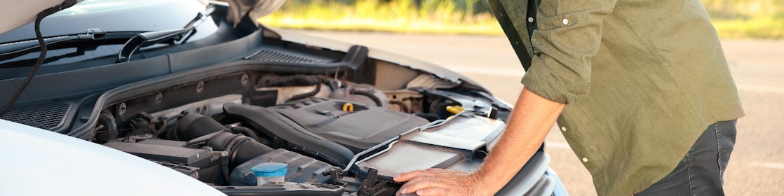 A man in a safety vest is positioned next to a white car, engaged in the process of charging an electric vehicle.