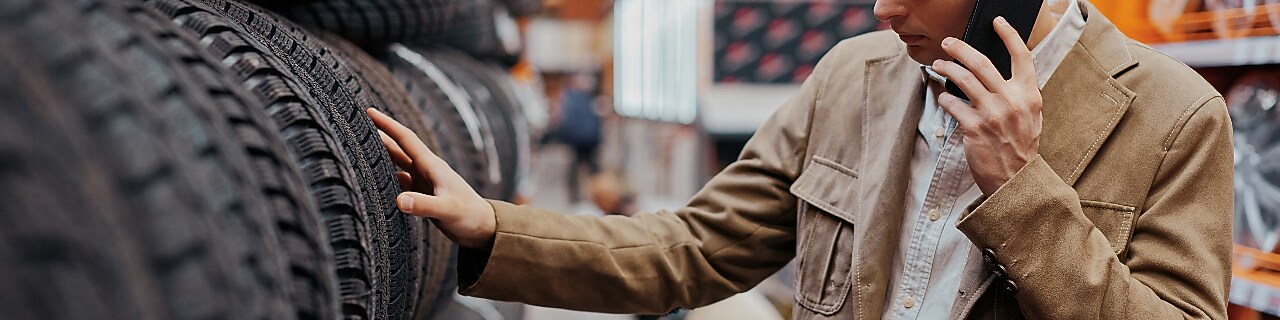 A man examines a tire while standing in a store, showcasing his interest in purchasing a new tire.