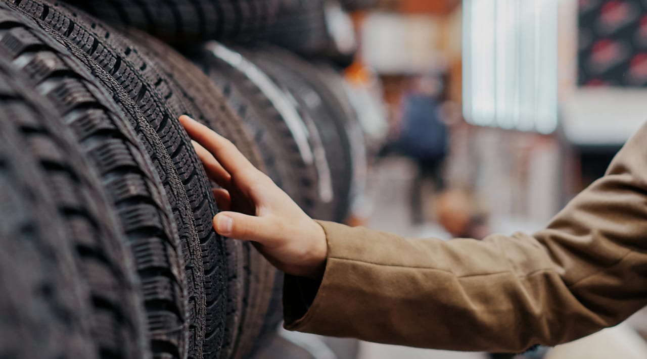 A man examines a tire while standing in a store, showcasing his interest in purchasing a new tire.