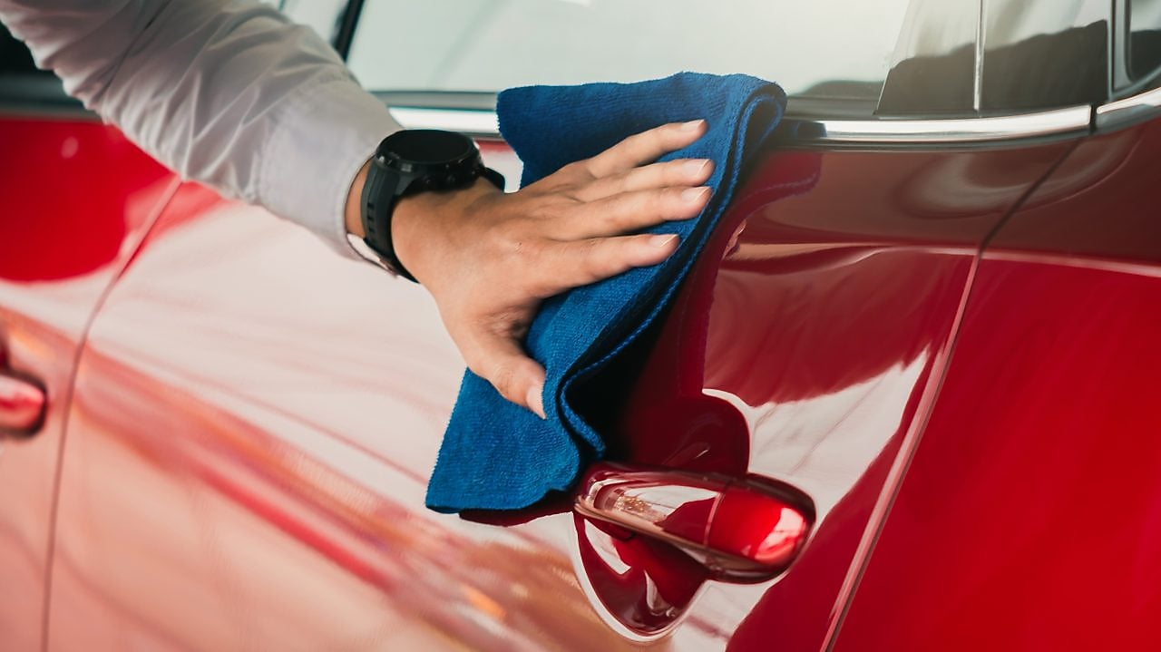 A man wipes down a red car door