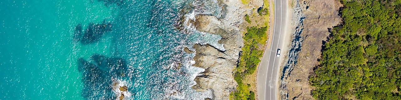 Aerial view of a car driving along the Great Ocean Road on a sunny day.