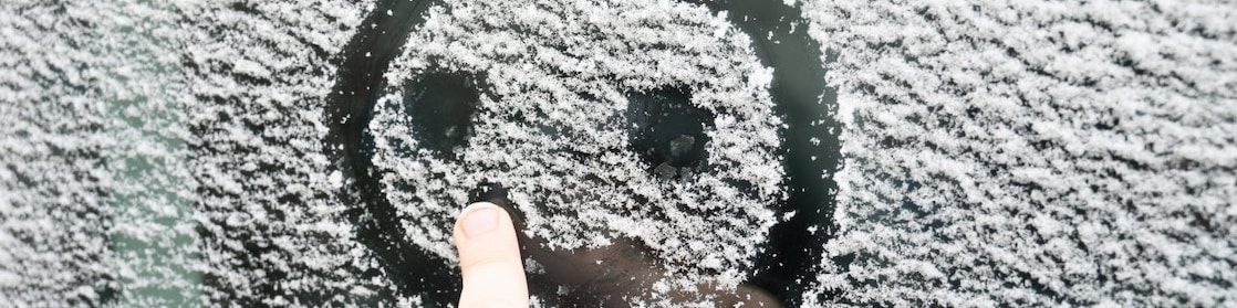 A child draws a smiling face in the ice on a car windshield.