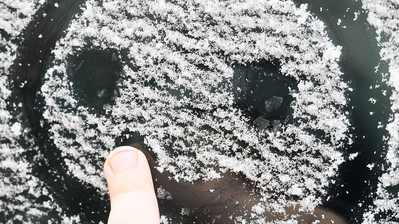 A child draws a smiling face in the ice on a car windshield.