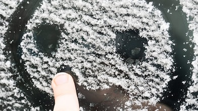A child draws a smiling face in the ice on a car windshield.
