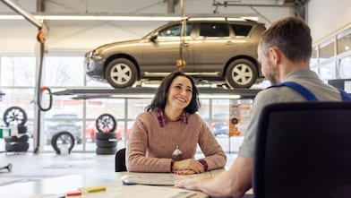 Happy and satisfied female customer discussing with service station manager. Woman talking with auto repair shop worker sitting in office.