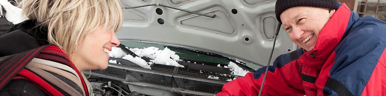 A man helps a woman jump start her battery in snowy weather.