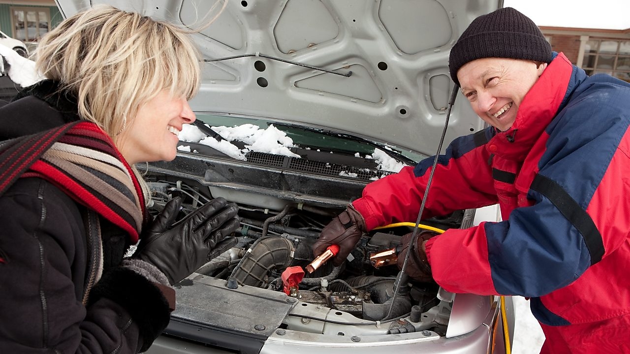 A man helps a woman jump start her battery in snowy weather.