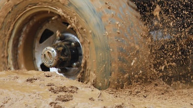 A yellow utility vehicle with its wheels bogged in mud.