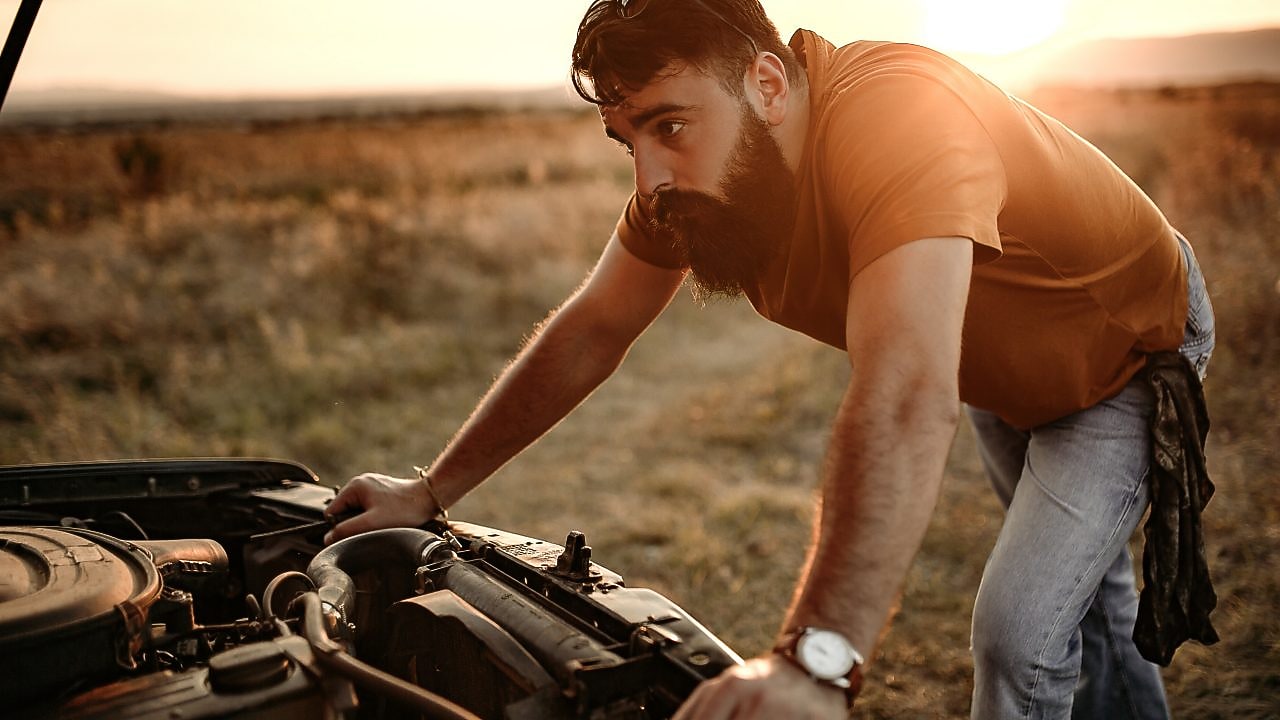 A man inspects his engine by the side of the road at sunset.