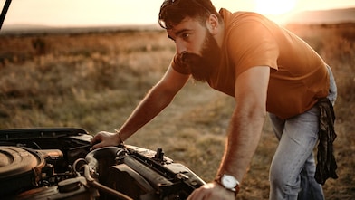 A man inspects his engine by the side of the road at sunset.