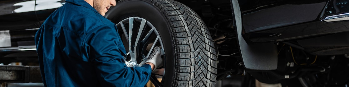 Young mechanic installing wheel on raised car in workshop