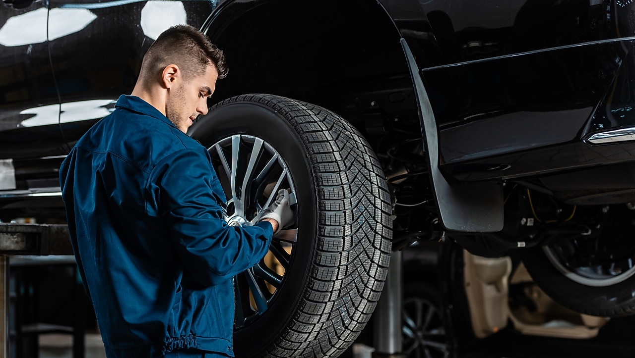 Young mechanic installing wheel on raised car in workshop