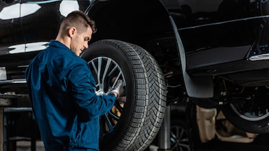 Young mechanic installing wheel on raised car in workshop