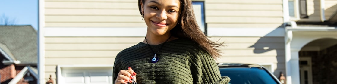 Woman standing at the bonnet of the car and holding keys in her hand