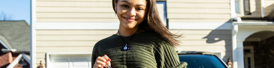 Woman standing at the bonnet of the car and holding keys in her hand