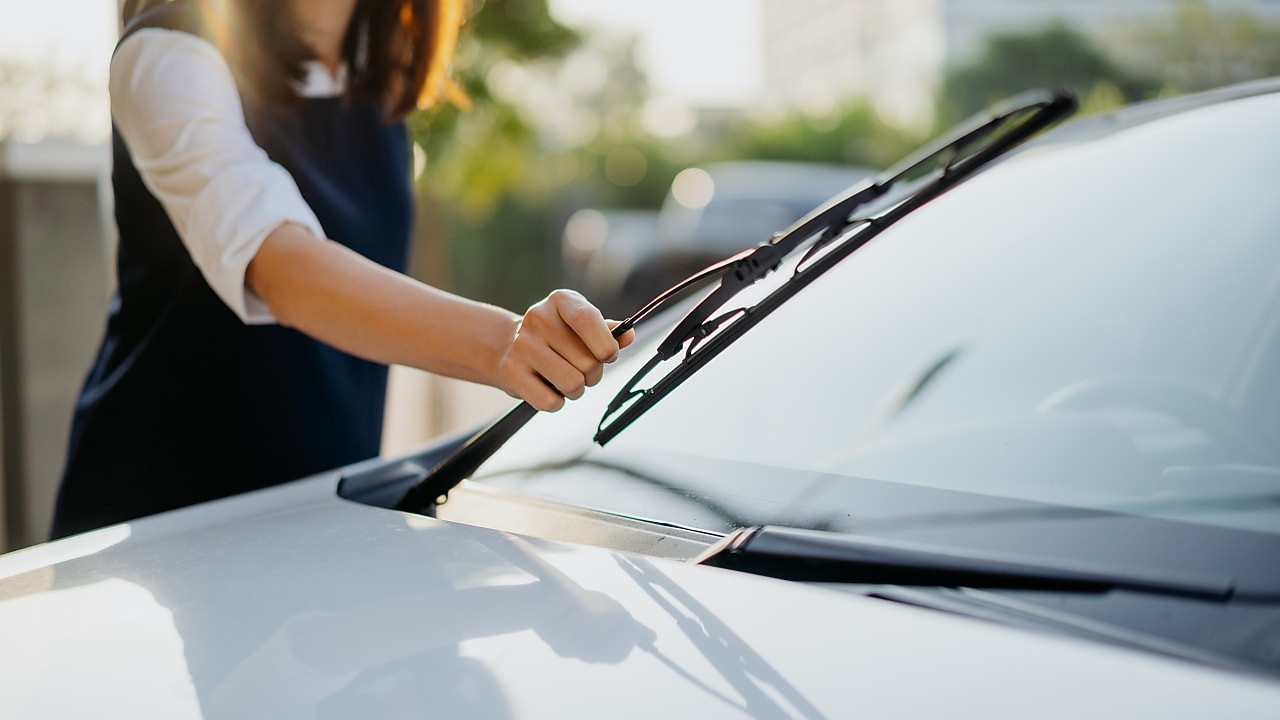 Image of an Asian woman checking her windshield wipers before her journey.