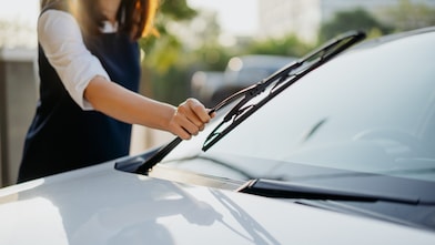 Image of an Asian woman checking her windshield wipers before her journey.