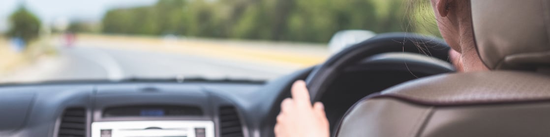 The girl is driving on the highway in Australia. View from the back seat of the car on the windshield, road and the driver