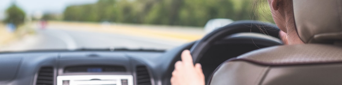 The girl is driving on the highway in Australia. View from the back seat of the car on the windshield, road and the driver