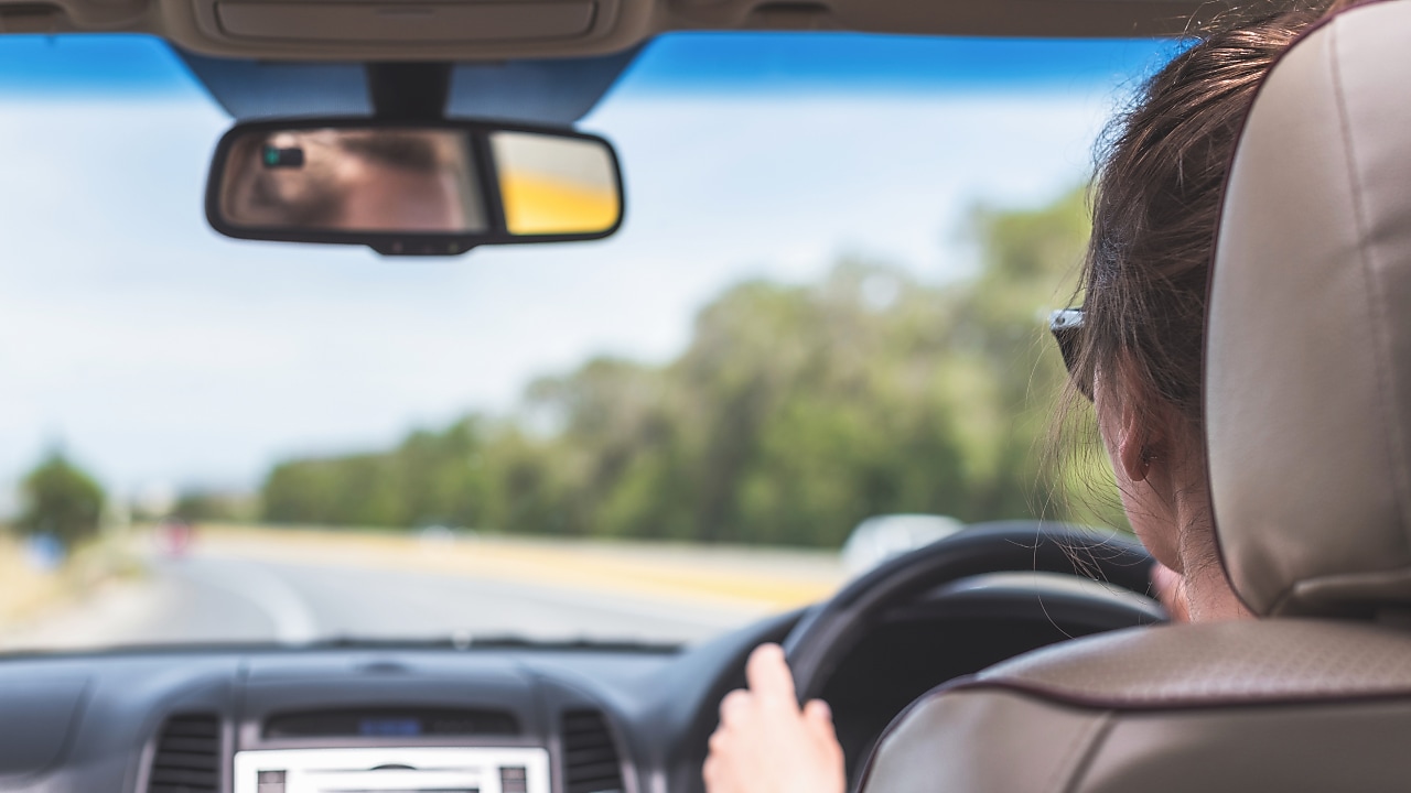 The girl is driving on the highway in Australia. View from the back seat of the car on the windshield, road and the driver