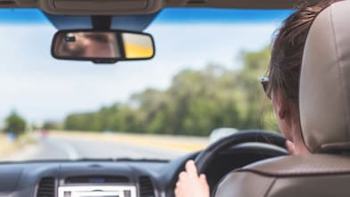 The girl is driving on the highway in Australia. View from the back seat of the car on the windshield, road and the driver