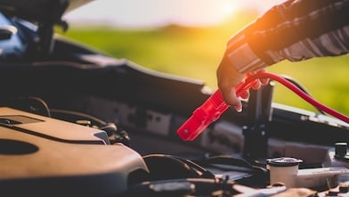 A woman connects red jumper leads to a car battery
