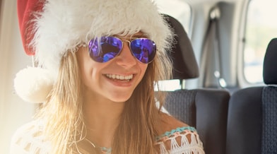 Three children in a car, wearing Santa hats and sunglasses, enjoying a festive ride together.