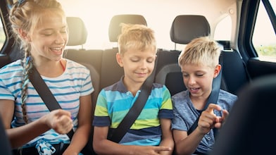 Three kids playing games in the car on a road trip