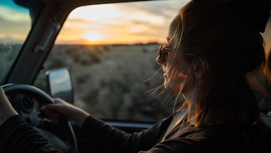 Young Woman drives car on sunset with window down