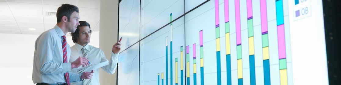 Business men analyse reports displayed on a large digital screen